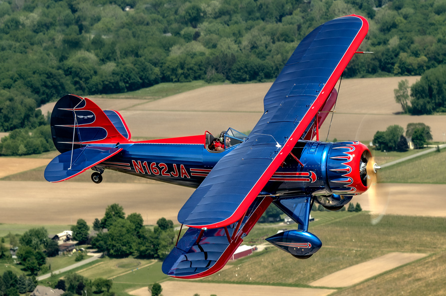 WACO YMF5 plane flying above fields and trees