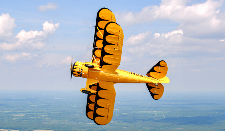 A bright yellow YMF-5 from WACO Aircraft flies through the air